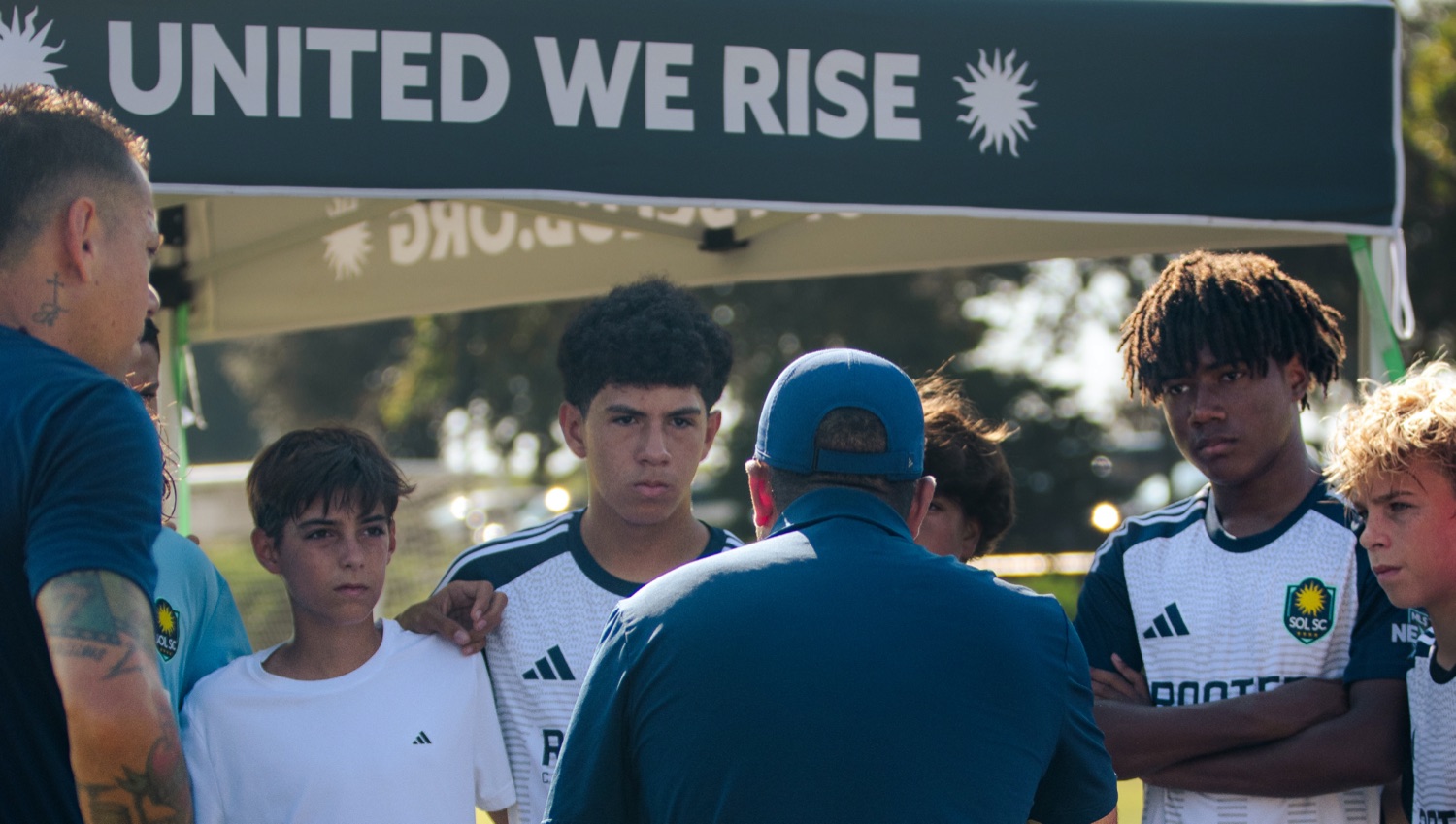 Sol SC MLS NEXT Academy team huddle under the United We Rise banner